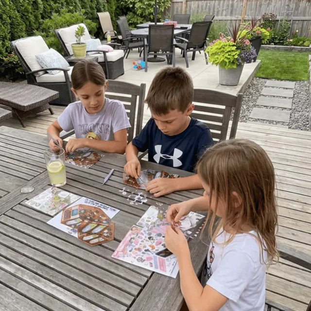Three children building GOODVIBESUMMER miniature scenes together at an outdoor table